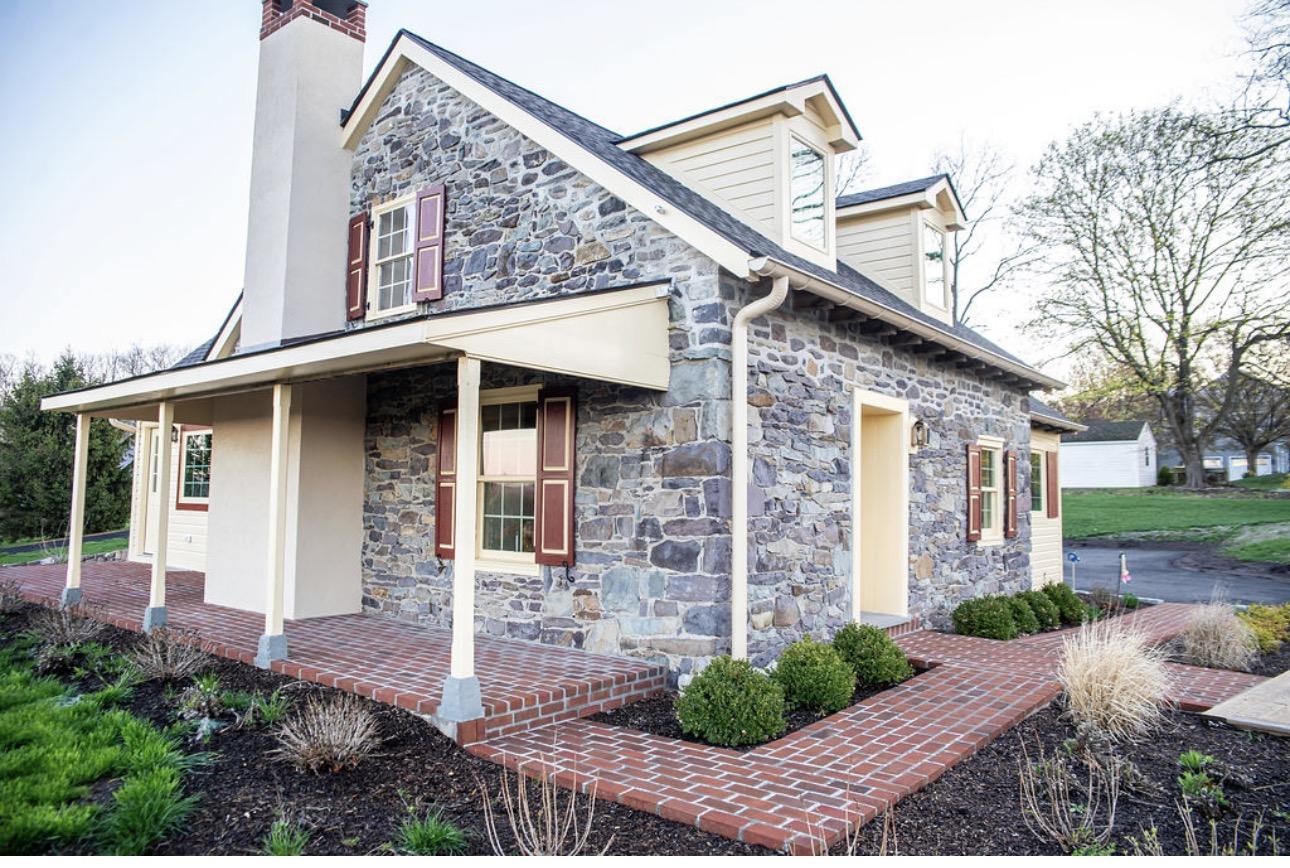 The stone cottage exterior with red shutters and a wraparound porch